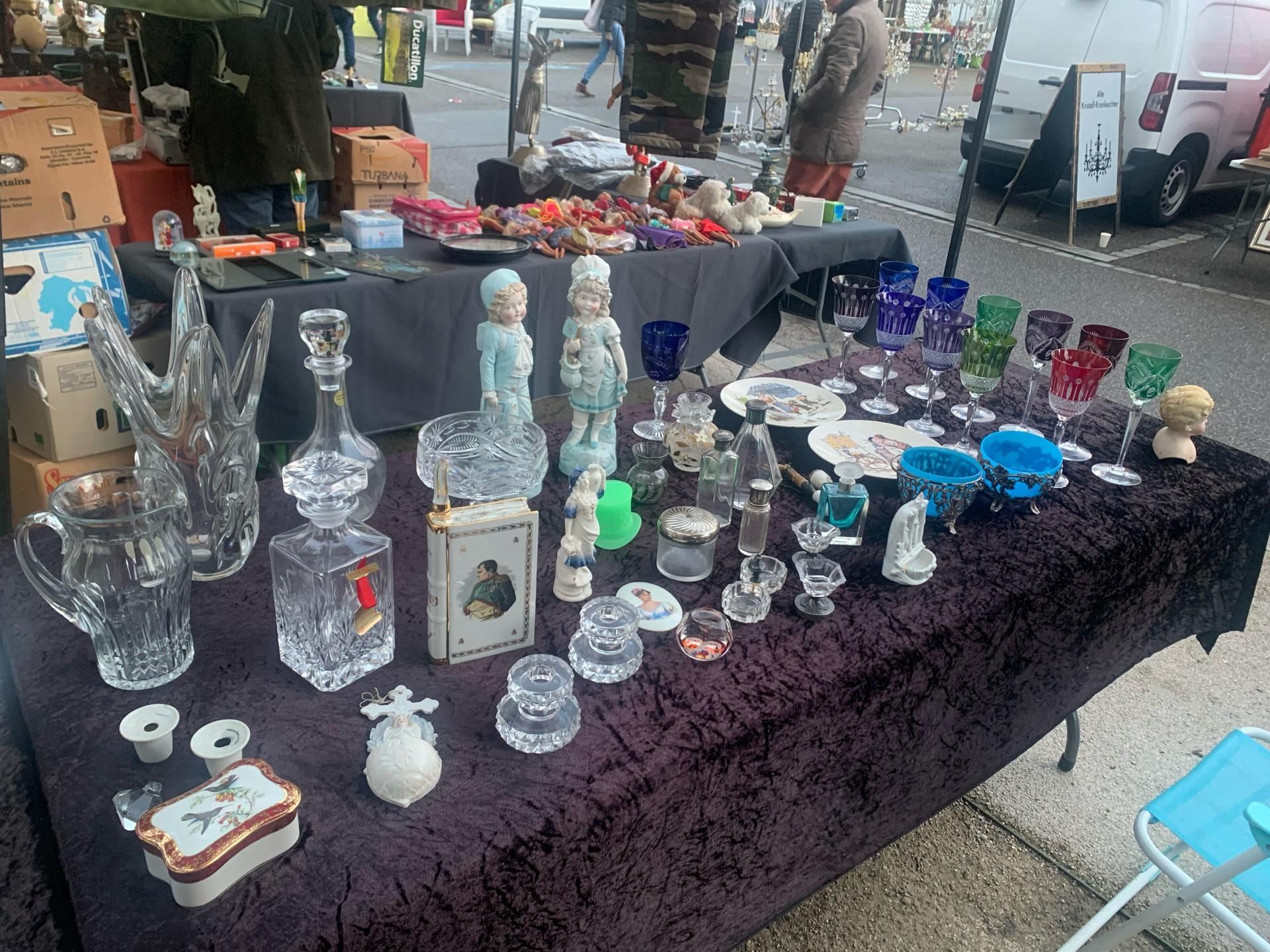 Sur une table, on trouve un assortiment de verrerie, de figurines et de bibelots à vendre