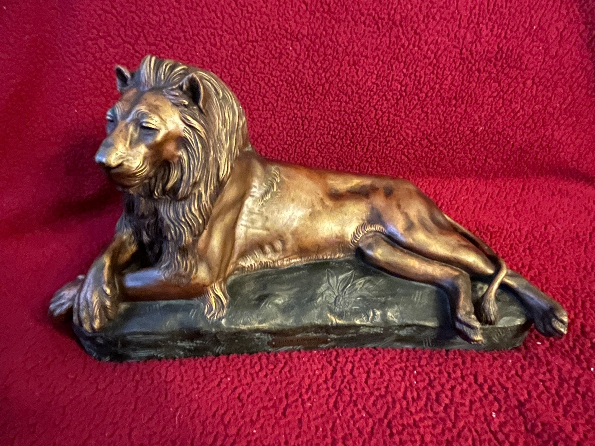 Statue de lion en bronze couché sur un socle en sombre sur fond de tissu rouge