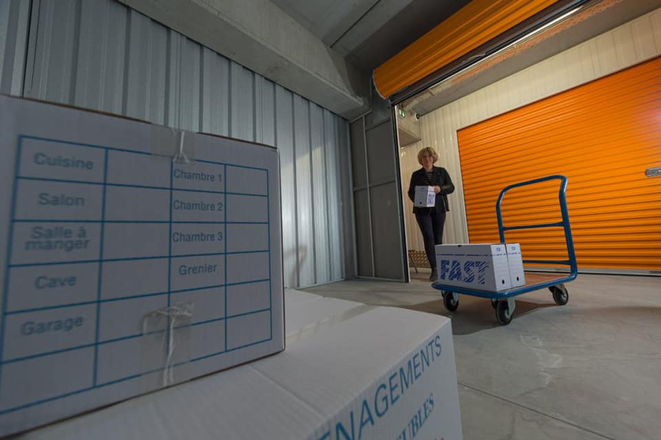 Femme avec un chariot qui entrepose des cartons dans un box