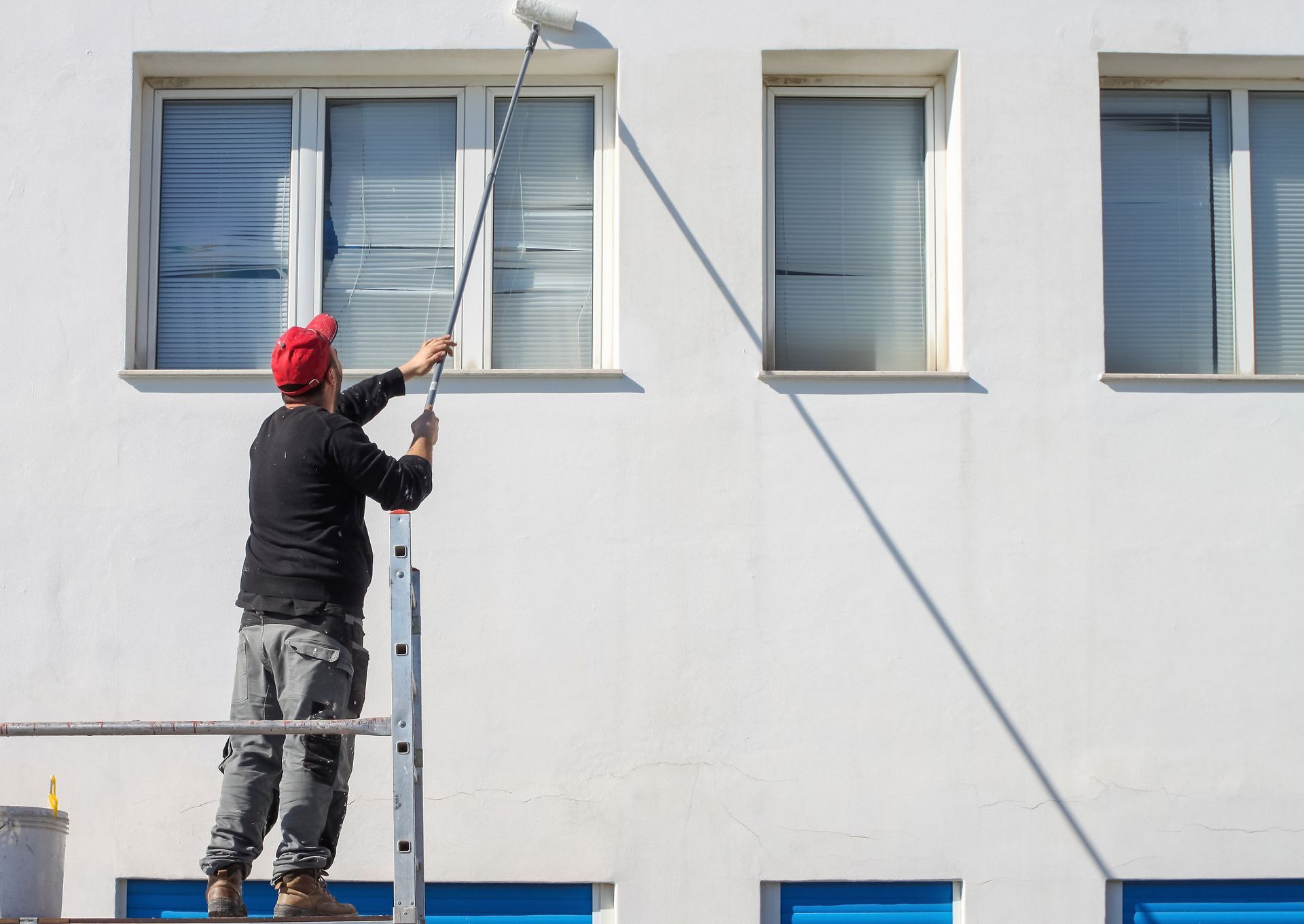 Un peintre qui peint une façade en blanc