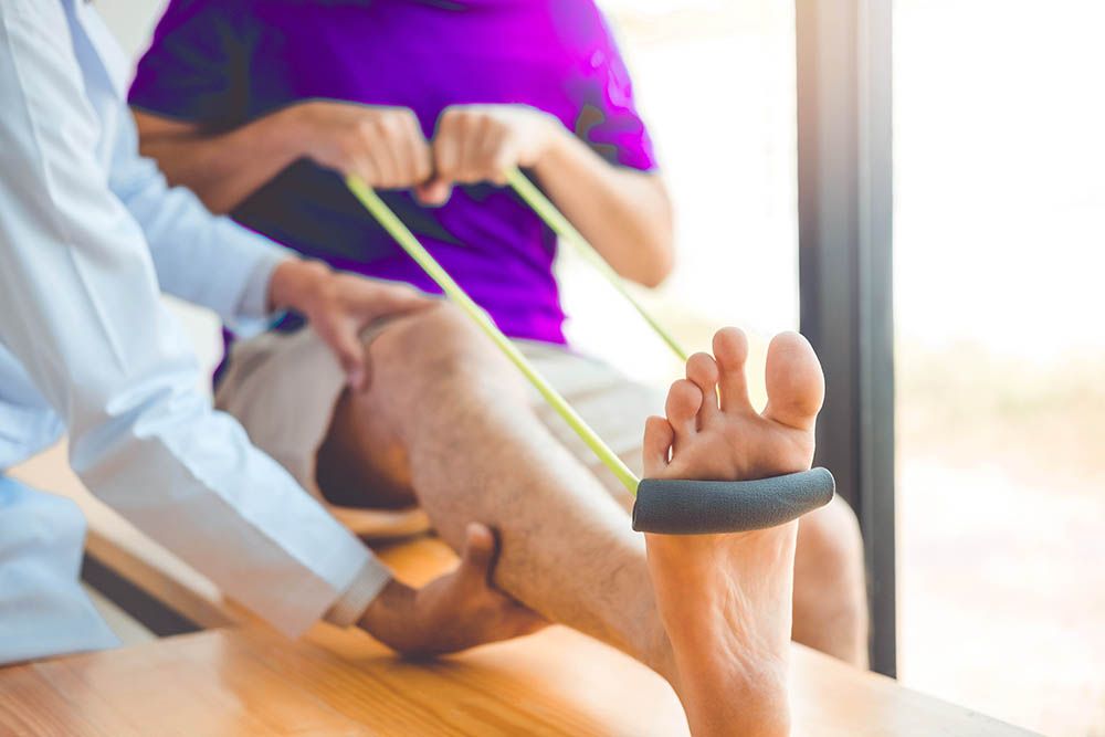 Ein Arzt dehnt den Fuß eines Patienten mit einem Gummiband.