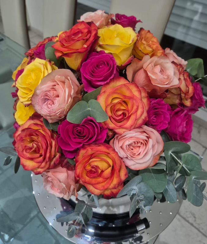 Bouquet de roses multicolores dans un vase argenté réfléchissant avec des feuilles d'eucalyptus.