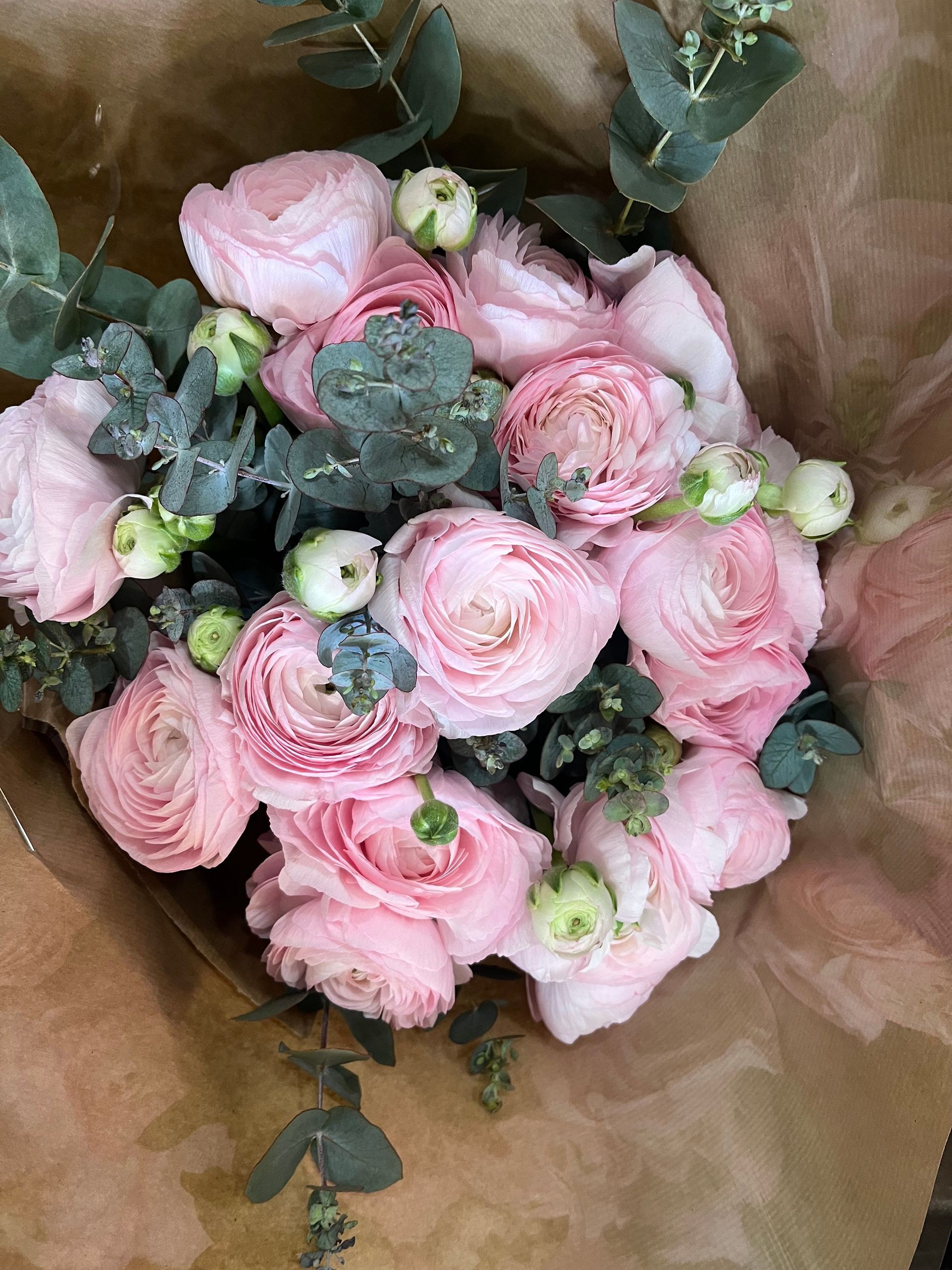 Bouquet de renoncules roses avec des baies blanches et de l'eucalyptus vert, emballé dans du papier kraft.