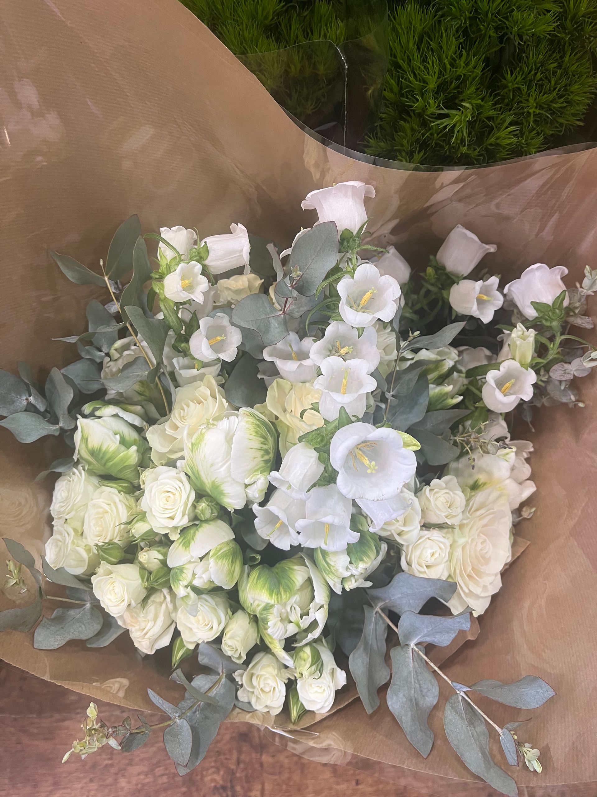 Bouquet de fleurs blanches et vert pâle enveloppé dans du papier brun, avec des feuilles d'eucalyptus bleu poudré.