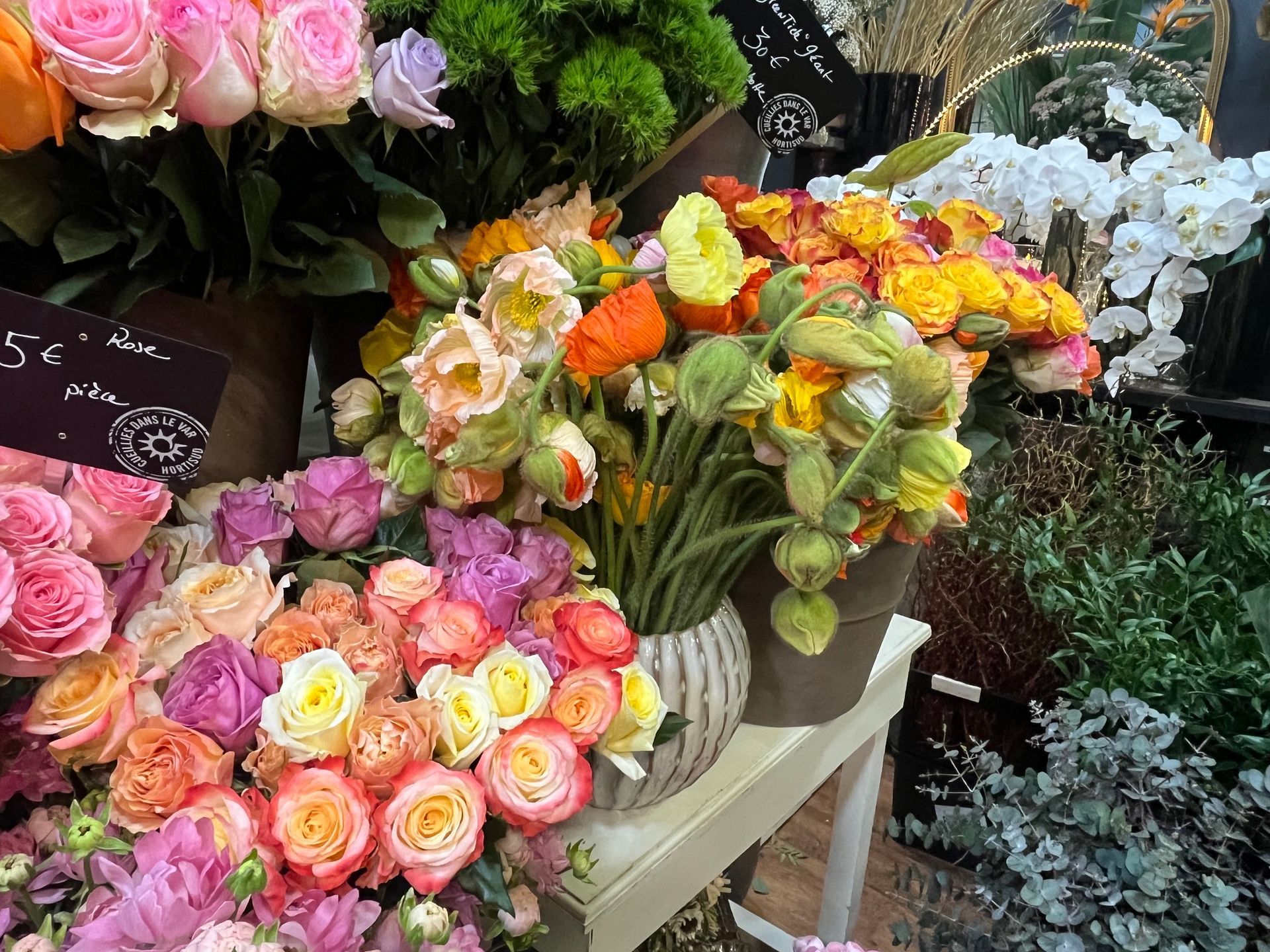 Des bouquets de roses et de fleurs aux couleurs variées sont présentés sur un étal de marché aux fleurs.