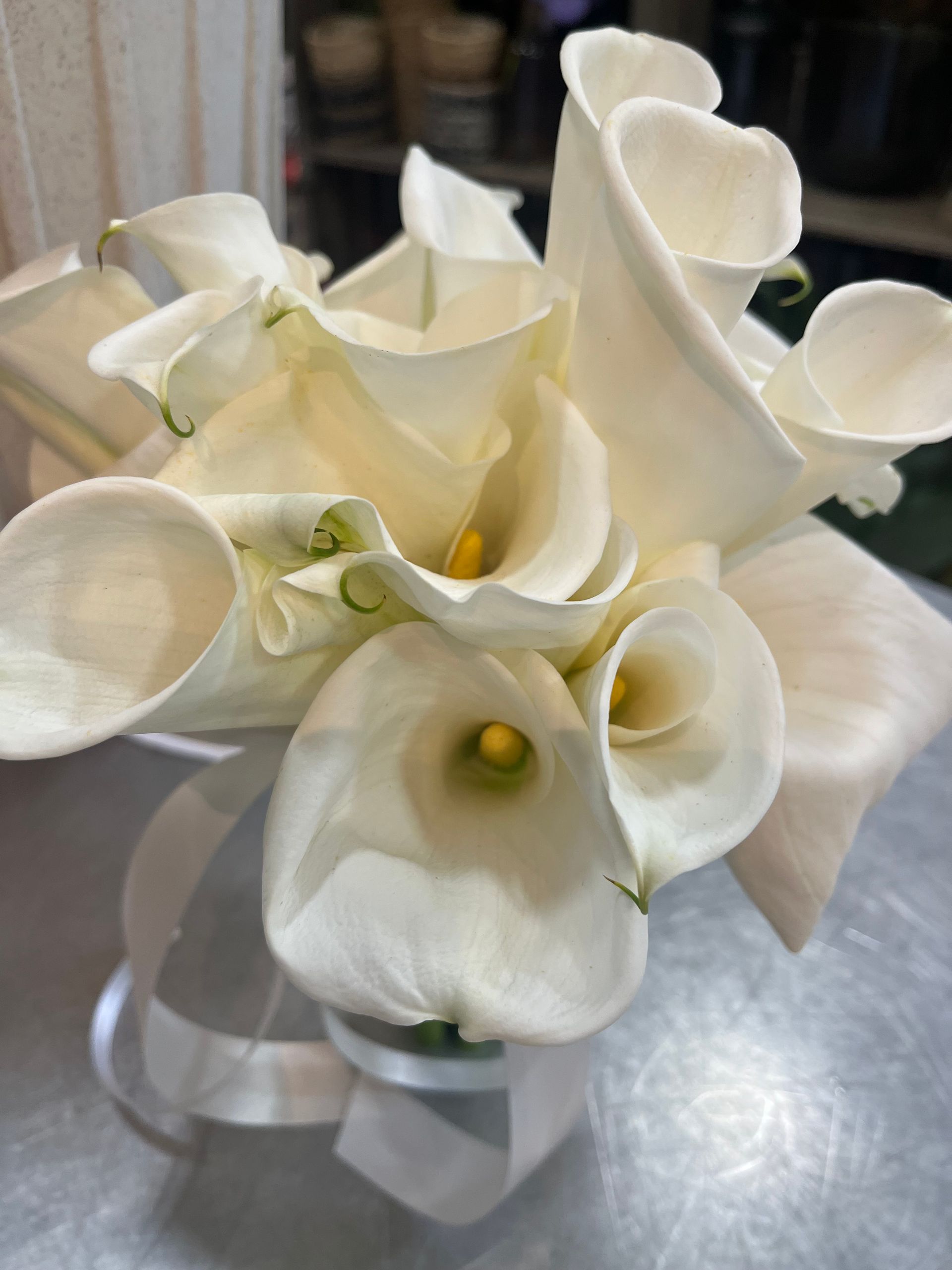 Bouquet de callas blanches avec ruban sur une table métallique.