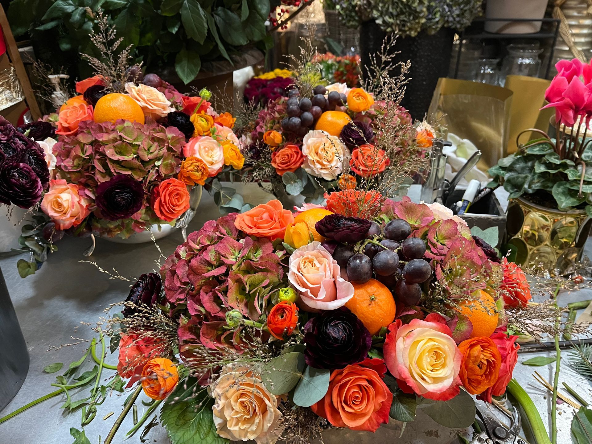 Des compositions florales éclatantes, avec des fleurs orange, roses et bordeaux, disposées sur une table.
