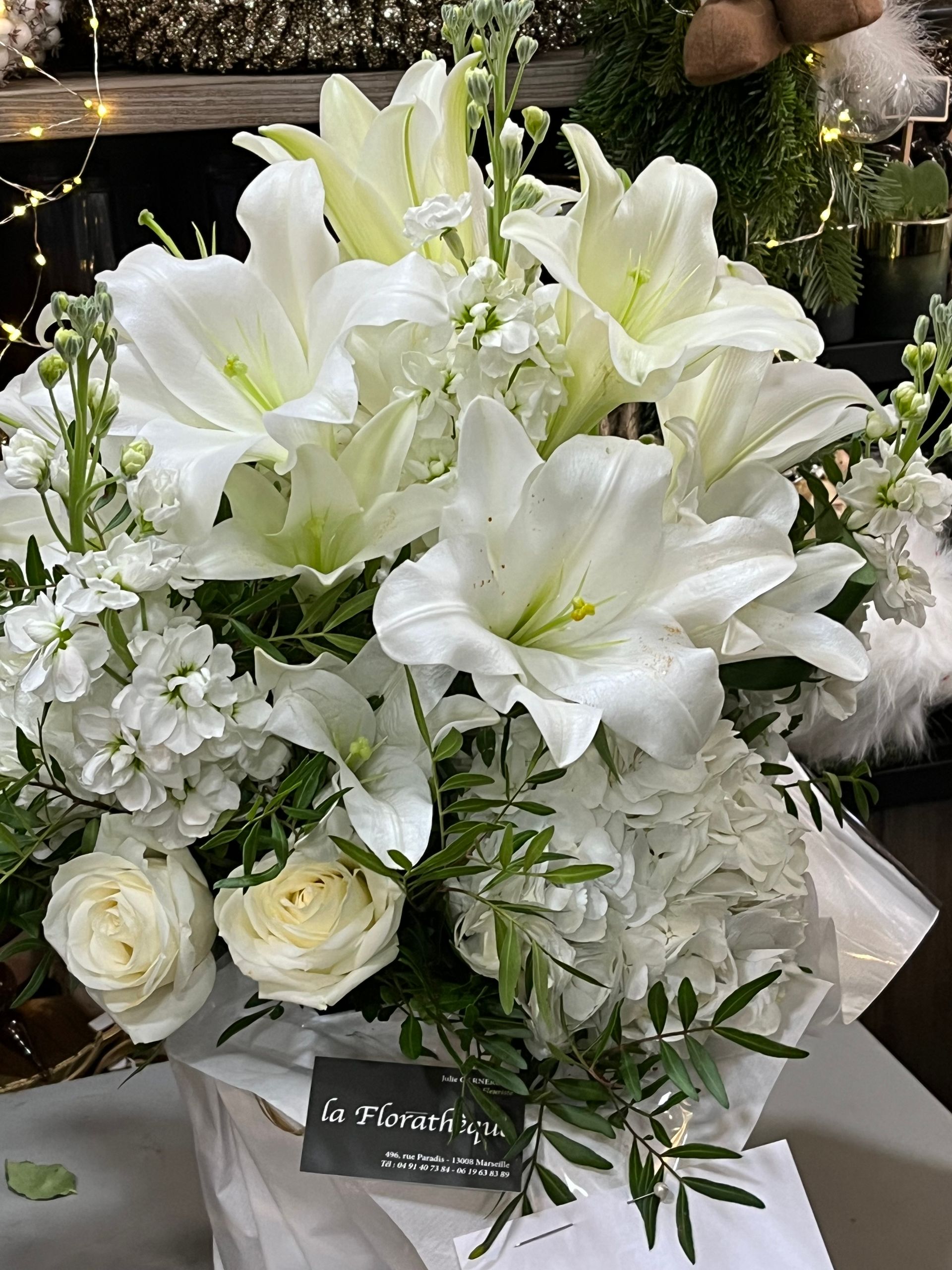 Un somptueux bouquet de fleurs composé de lys blancs et de roses, agrémenté de verdure et d'une carte.