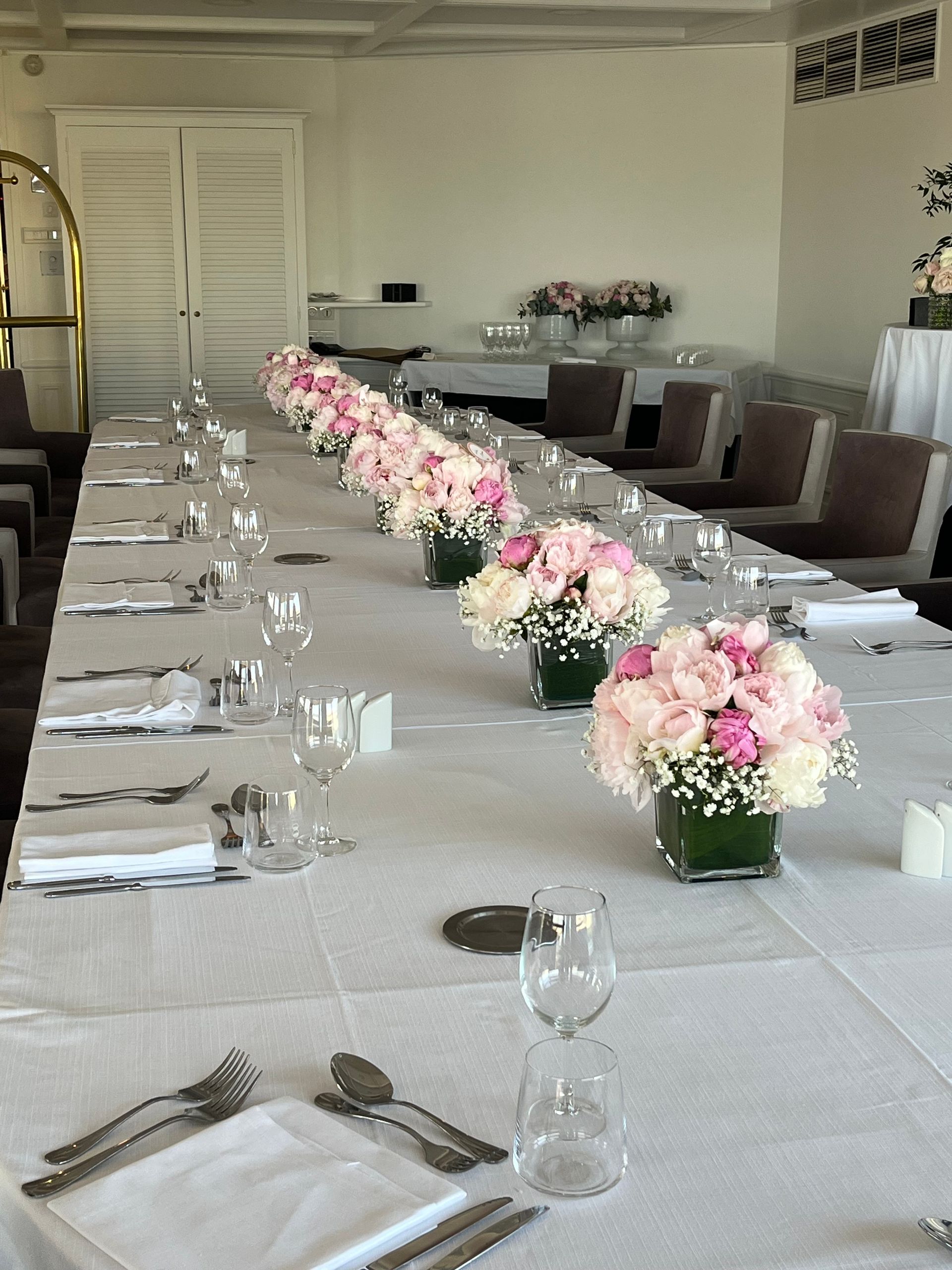 Longue table de banquet dressée avec des nappes blanches et des centres de table floraux roses.