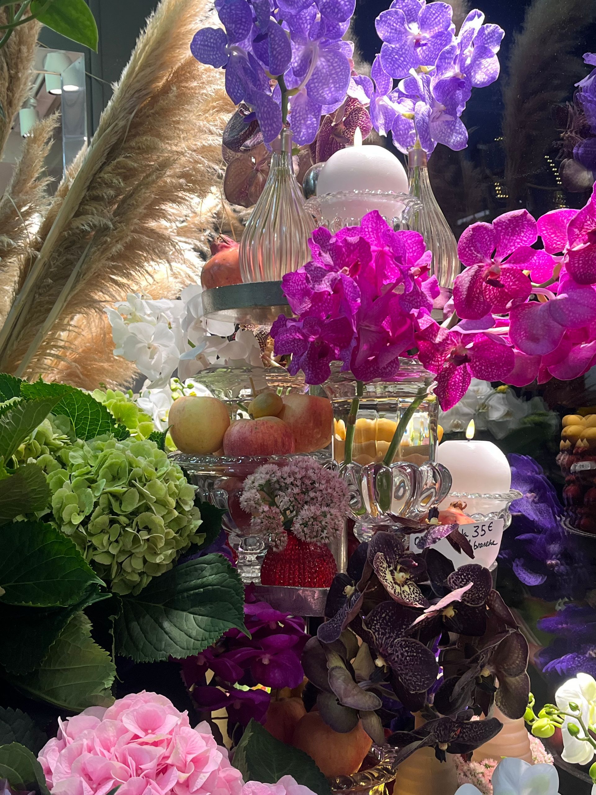 Composition florale colorée avec des fleurs violettes, roses et vertes et des éléments décoratifs en verre.