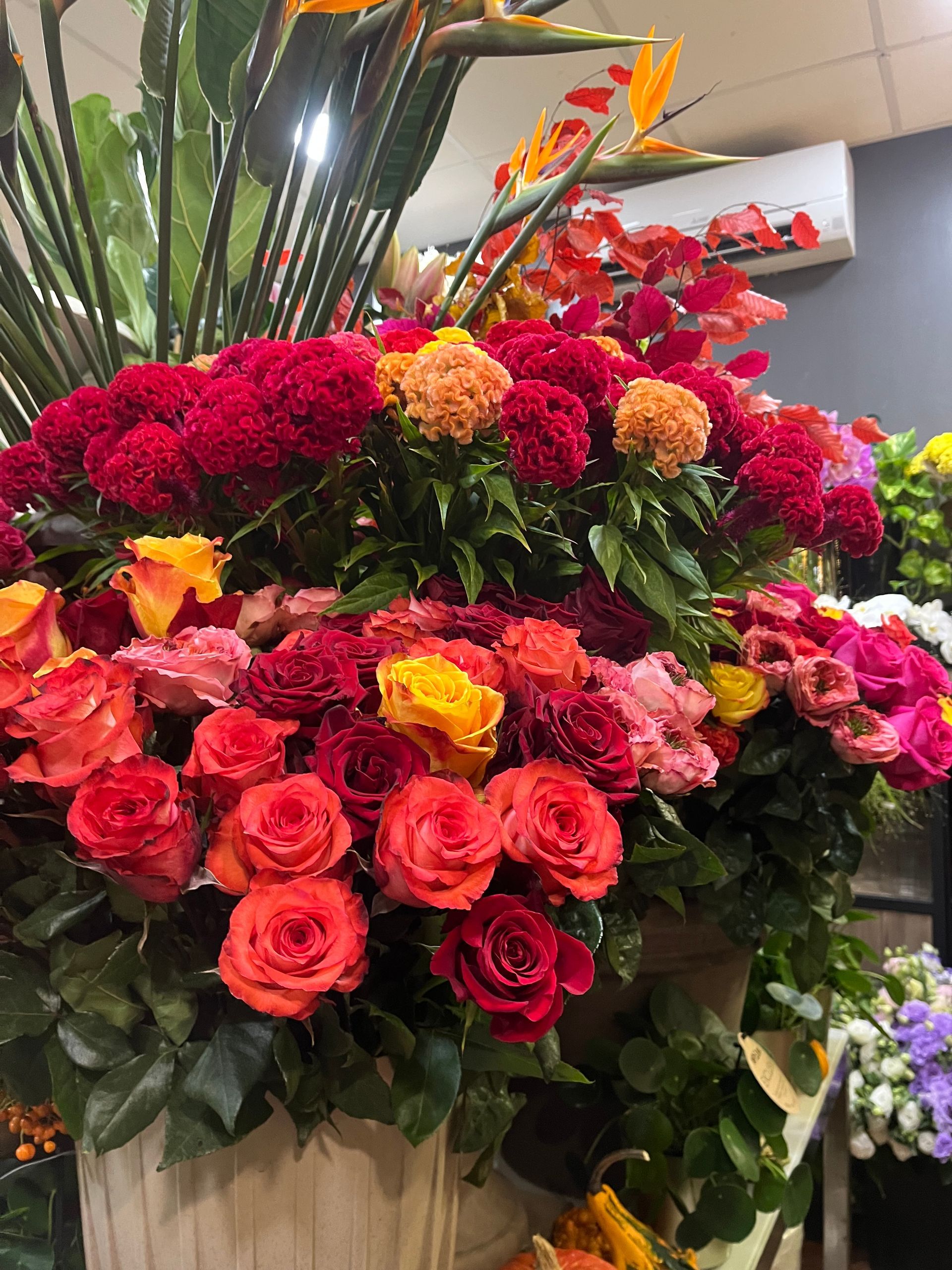 Grand arrangement floral coloré avec des fleurs rouges, roses, jaunes et oranges dans un panier décoratif.