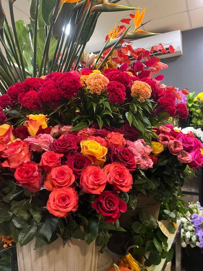 Grande composition florale avec des fleurs rouges, roses, oranges et jaunes dans une vitrine de magasin.