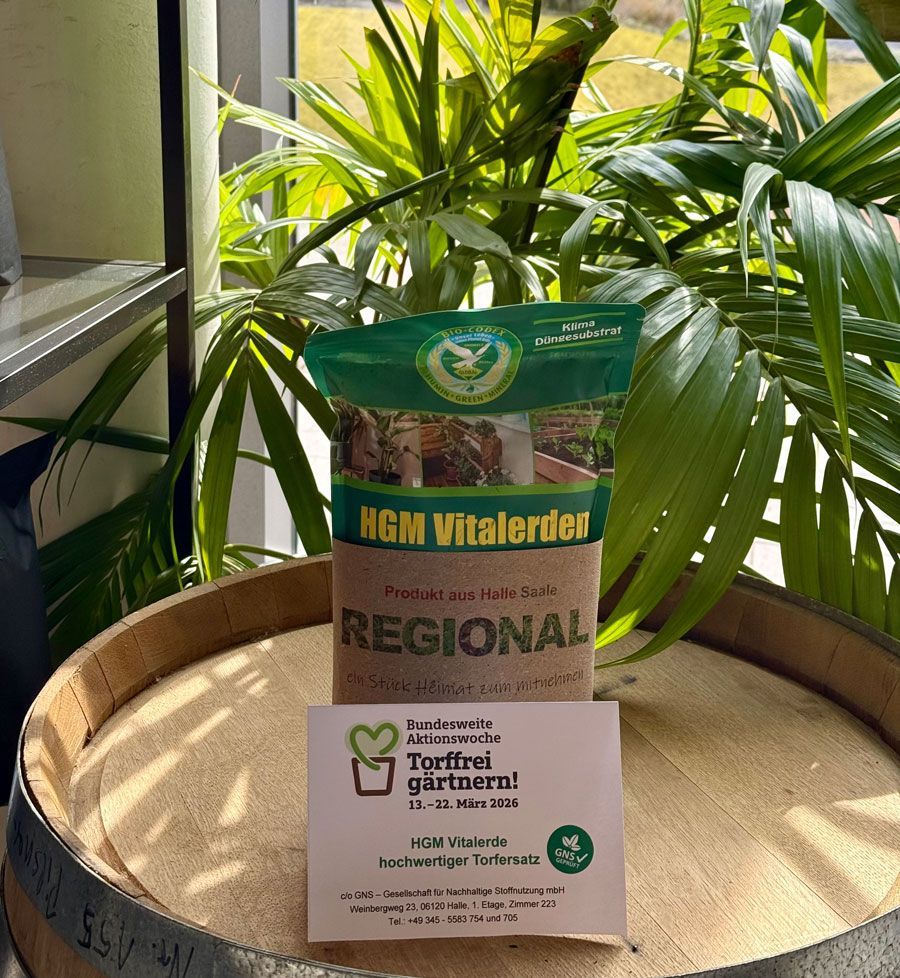 Fünf Personen sitzen um einen Tisch mit mehreren schwarzen Gegenständen. Sie scheinen sich in einem Raum mit großen Fenstern zu befinden.