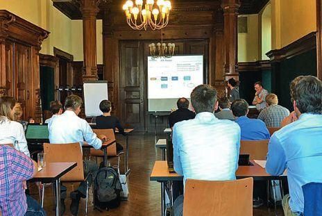 Eine Gruppe von Menschen sitzt an Tischen vor einer Projektionsleinwand.