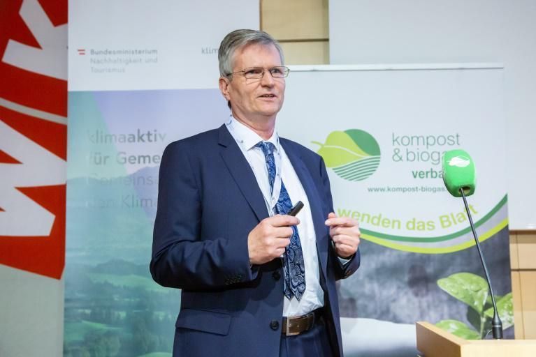 Ein Mann in Anzug und Krawatte hält vor einem Mikrofon eine Rede.