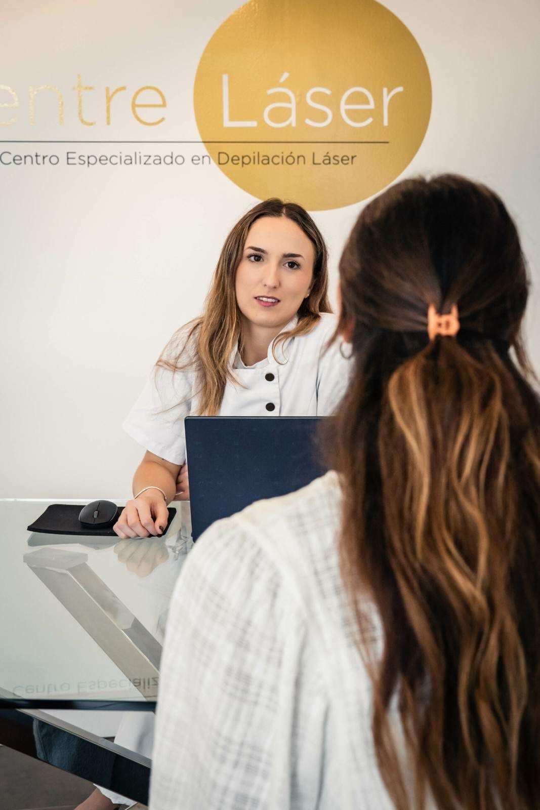 Recepción de una clínica de depilación láser, con un miembro del personal hablando con un cliente sentado.