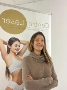 Mujer sonriente de pie frente a un cartel de Centro Láser con una mujer vestida con ropa deportiva blanca