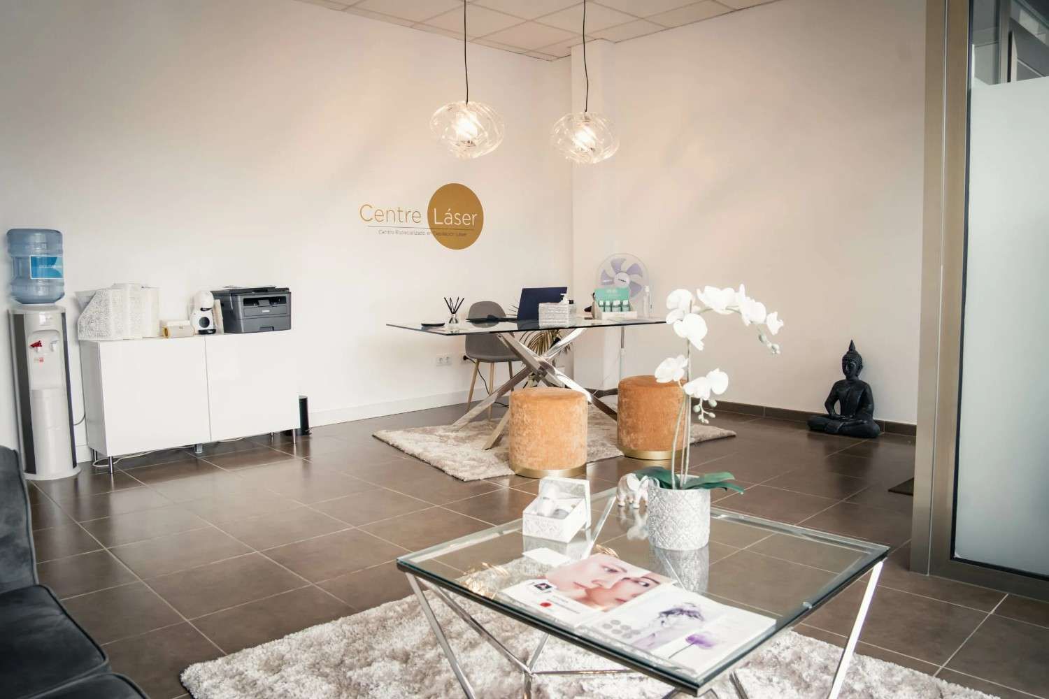 Moderno salón de oficina con mesa de centro de cristal, sillas, armario blanco y dispensador de agua