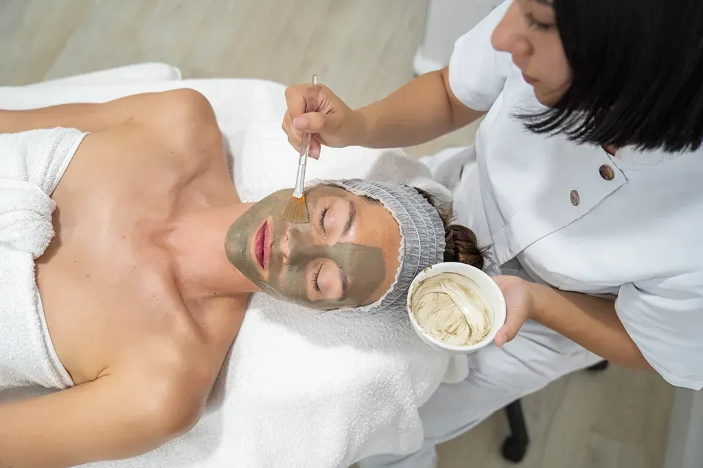Tratamiento facial de spa con una mascarilla verde aplicada a una persona tumbada en una camilla de tratamiento