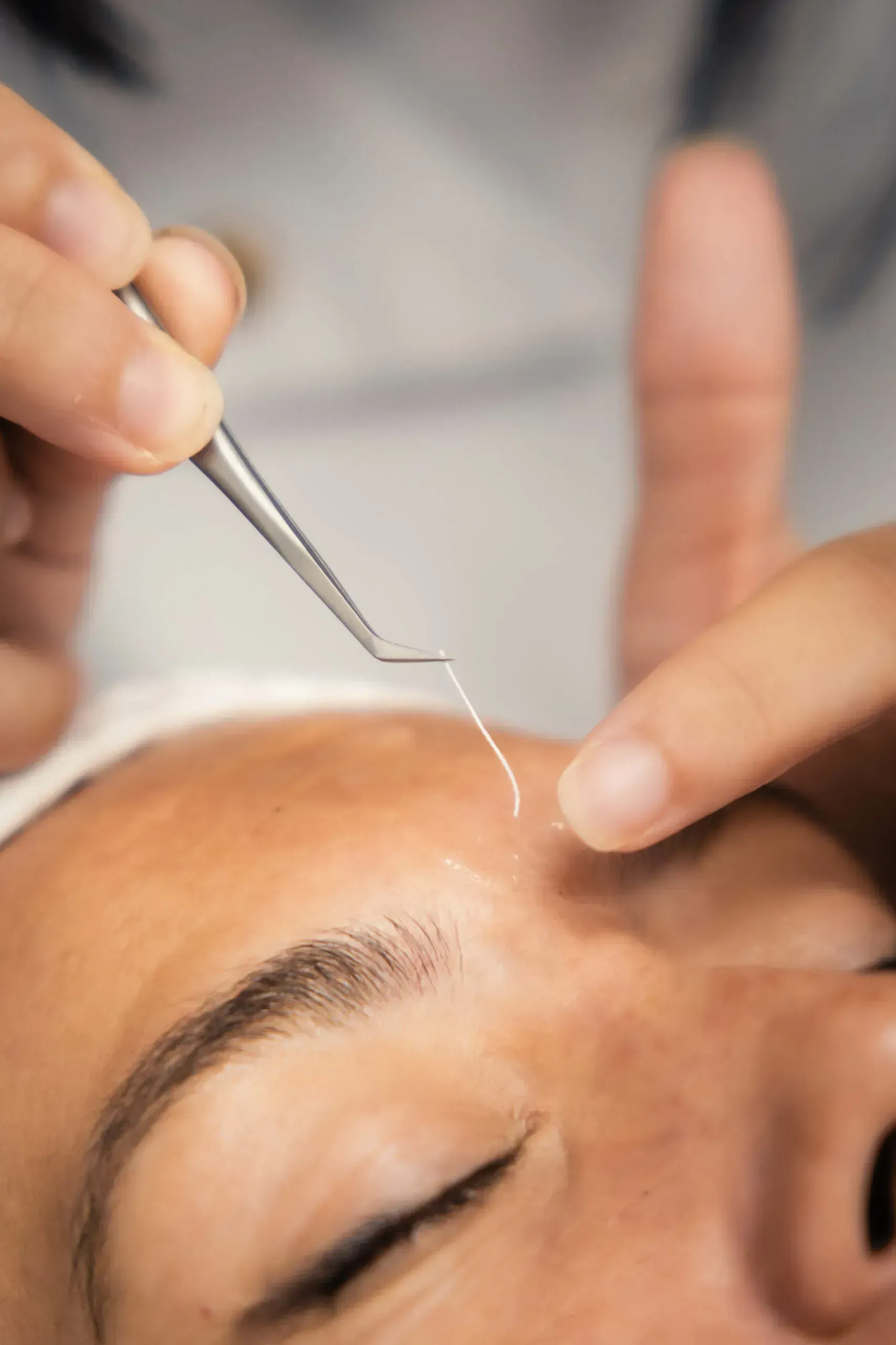 Unas pinzas aplicando un hilo fino a la ceja de una persona durante un tratamiento cosmético
