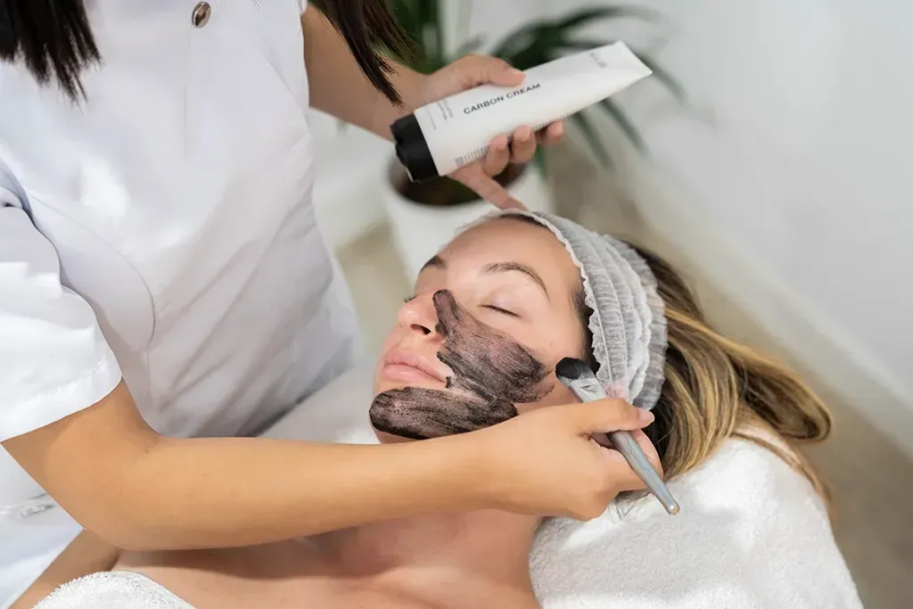 Un tratamiento facial con una mascarilla negra aplicada a un cliente reclinado en un spa