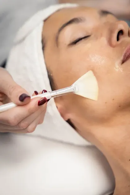 Tratamiento facial con un pincel aplicando un producto en la mejilla de una mujer mientras está tumbada en una camilla de spa