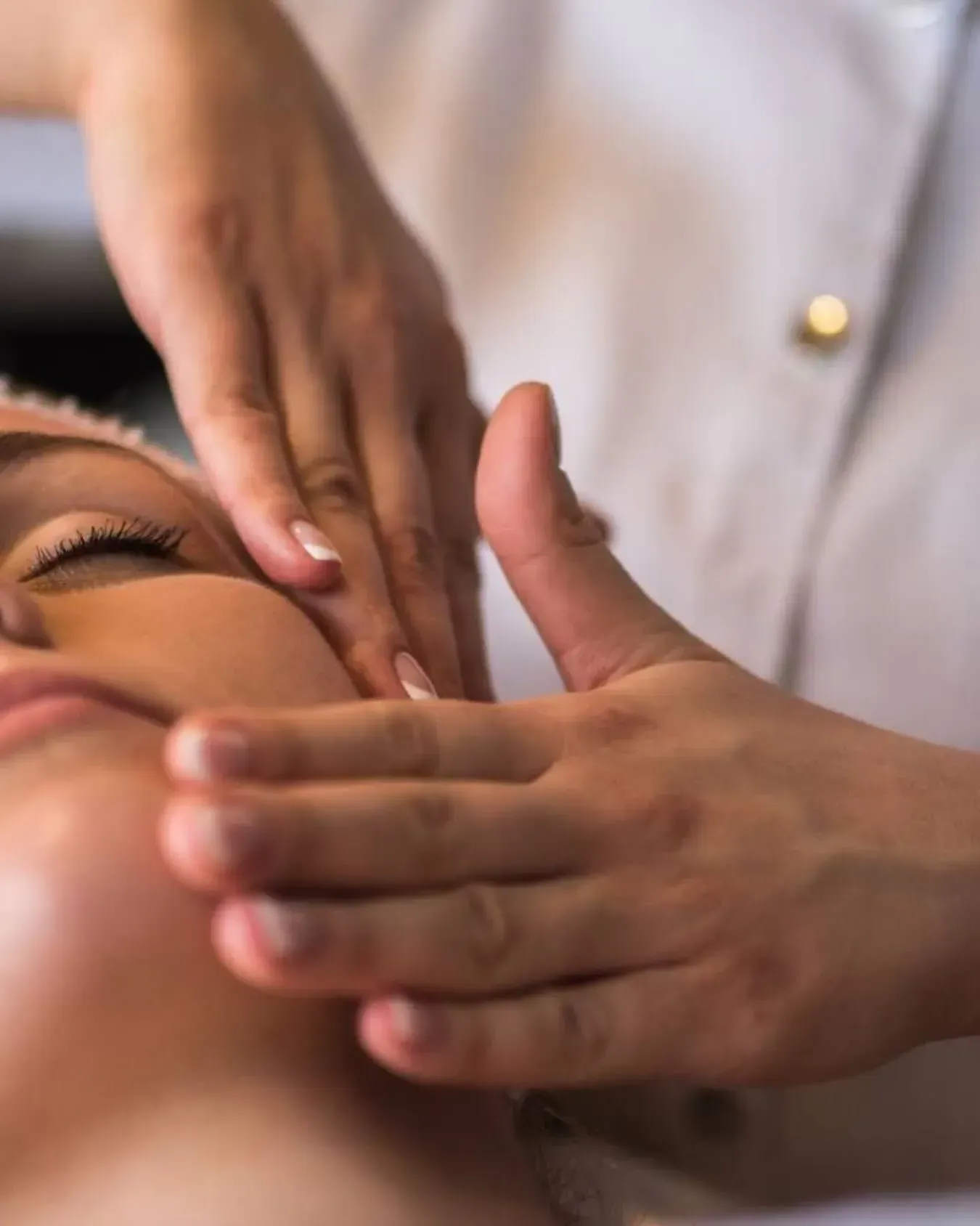 Manos aplicando un tratamiento facial cerca del ojo cerrado de una mujer en un spa