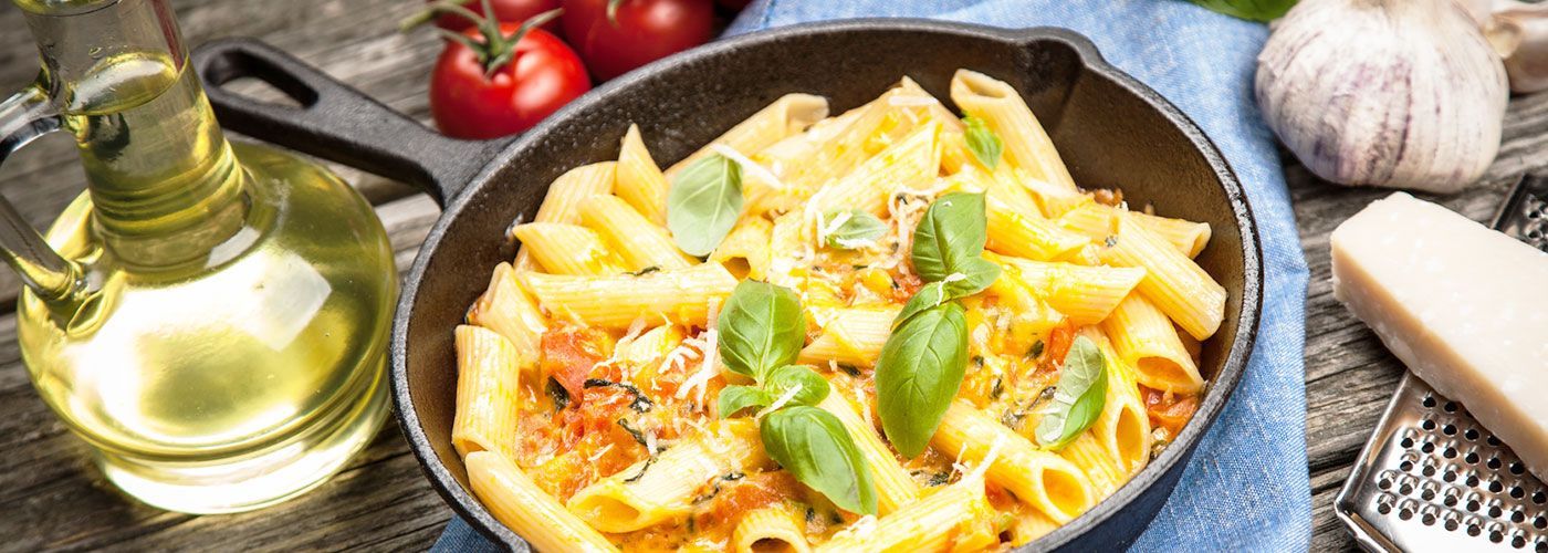 Eine Pfanne Nudeln mit Tomatensoße und Käse auf einem Holztisch.