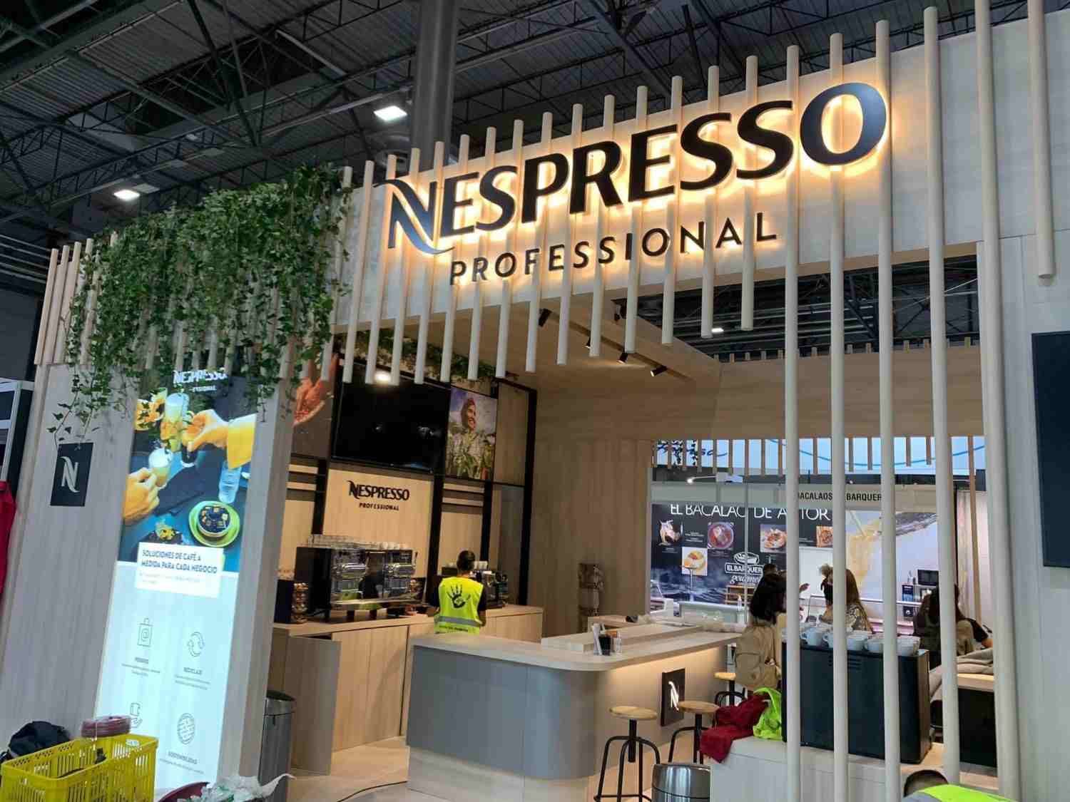 Stand de Nespresso Professional con mostrador y plantas colgantes en una feria comercial cubierta