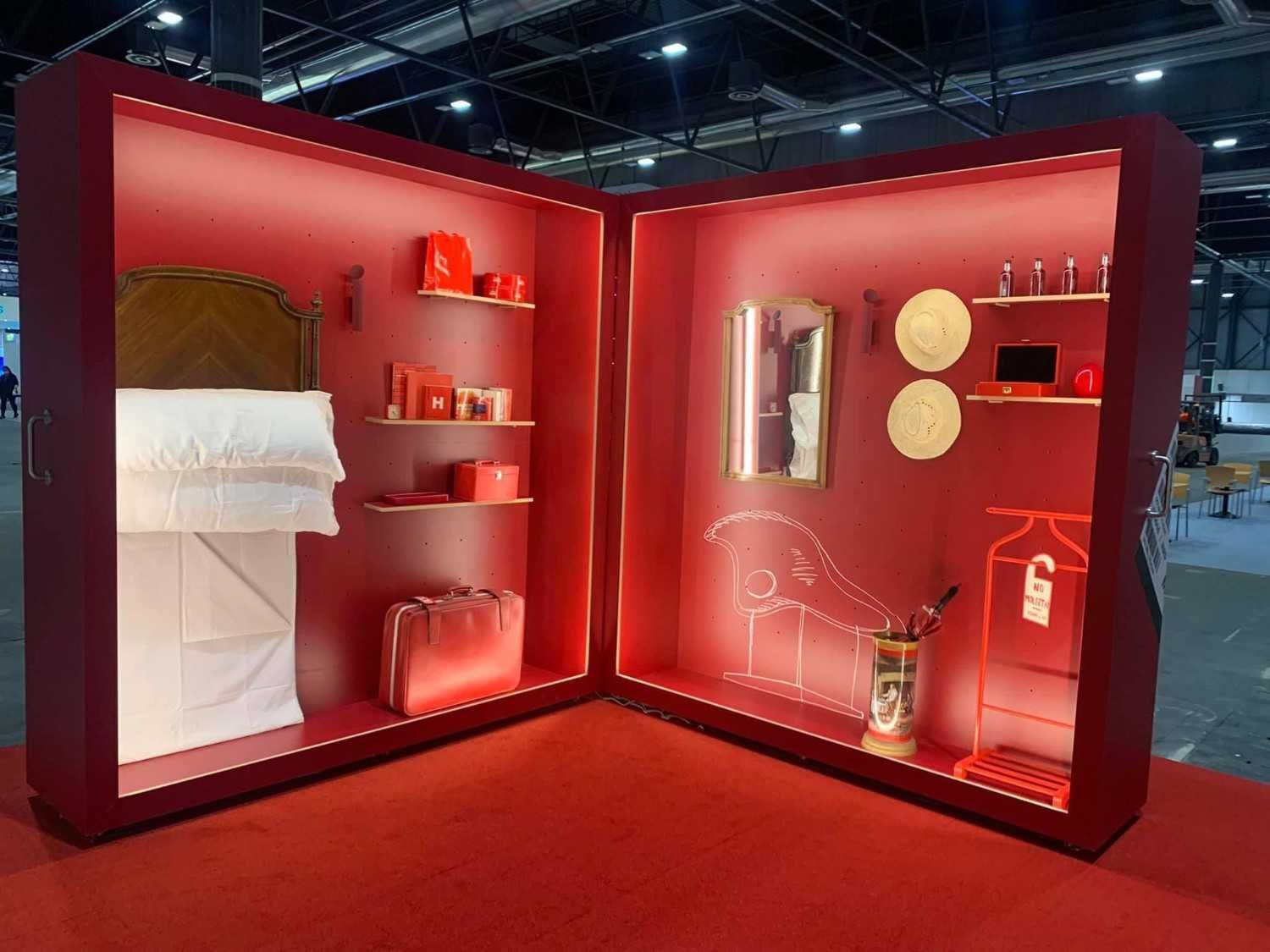 Stand de exposición rojo con camas, estanterías, espejos y elementos decorativos en una feria comercial