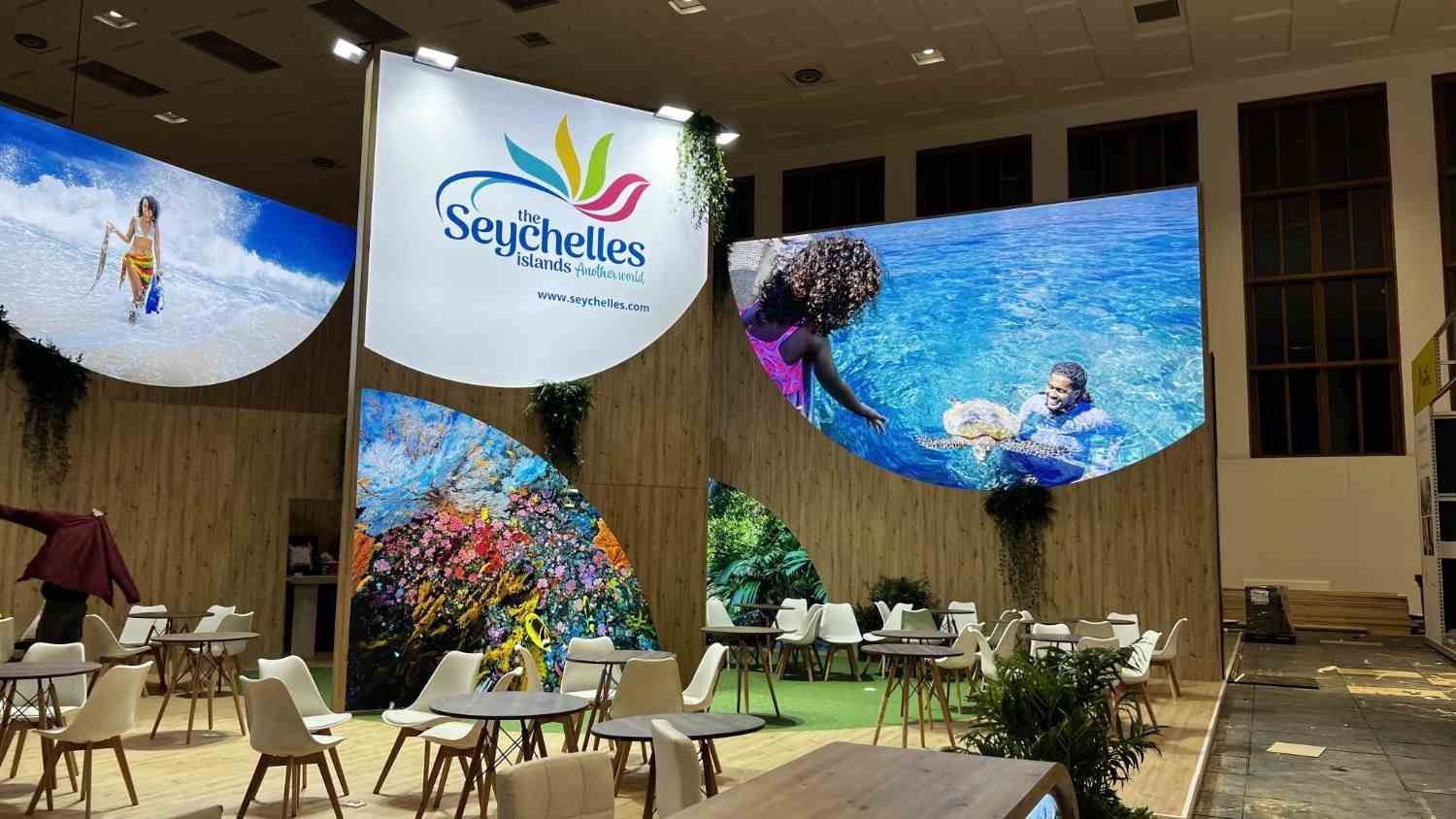 Zona de asientos con un expositor turístico de Seychelles y grandes pantallas coloridas con temática submarina