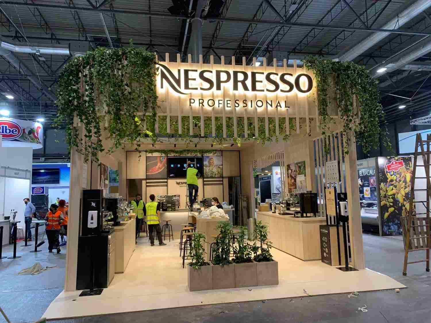Stand de Nespresso Professional en una feria, con detalles de madera, vegetación y personal atendiendo a los visitantes