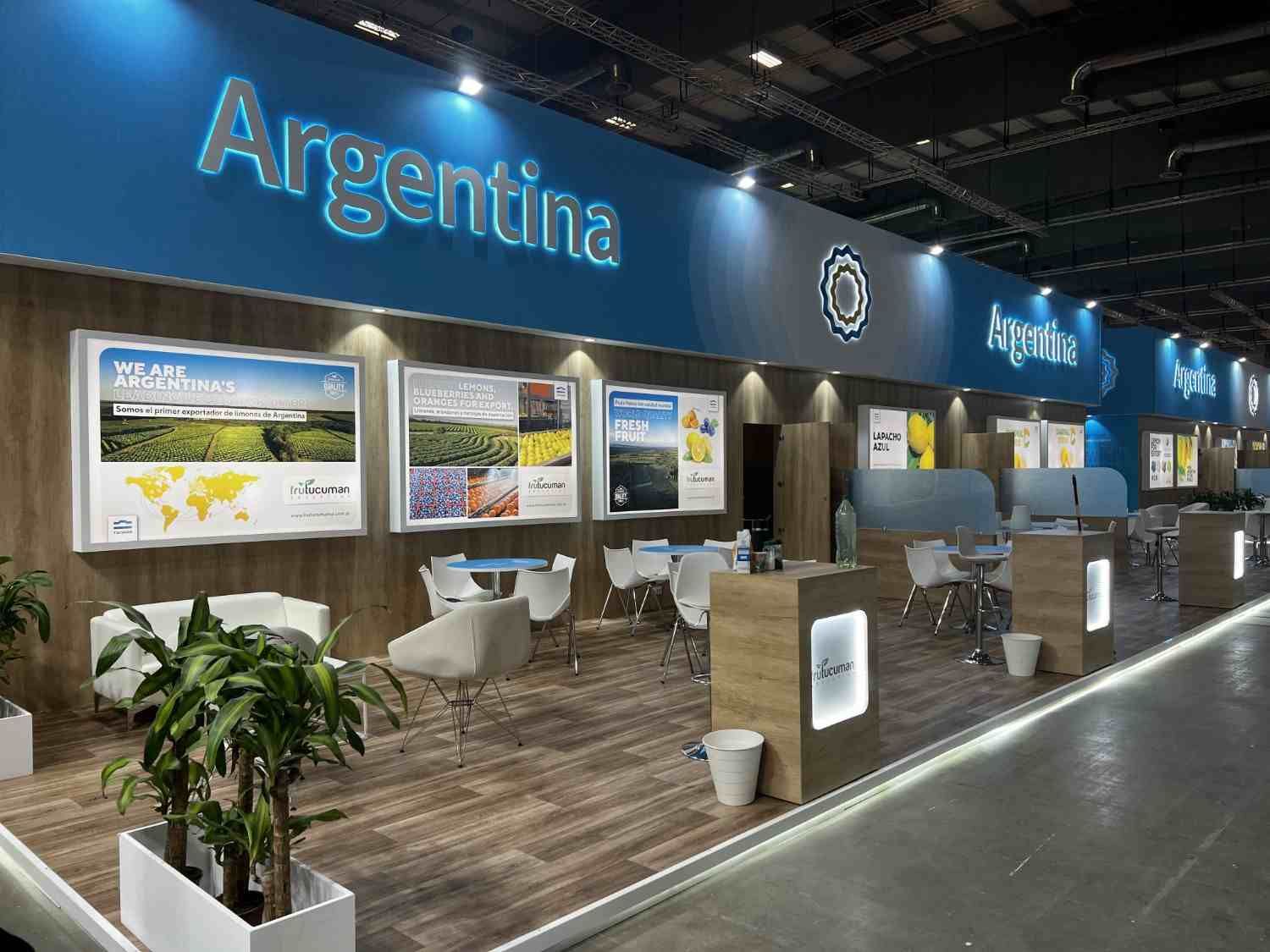 Stand de Argentina con carteles azules, pantallas iluminadas, mesas y sillas en un centro de convenciones