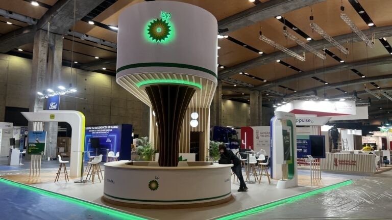 Stand de feria con una gran pantalla cilíndrica, iluminación verde y stands de exposición alrededor