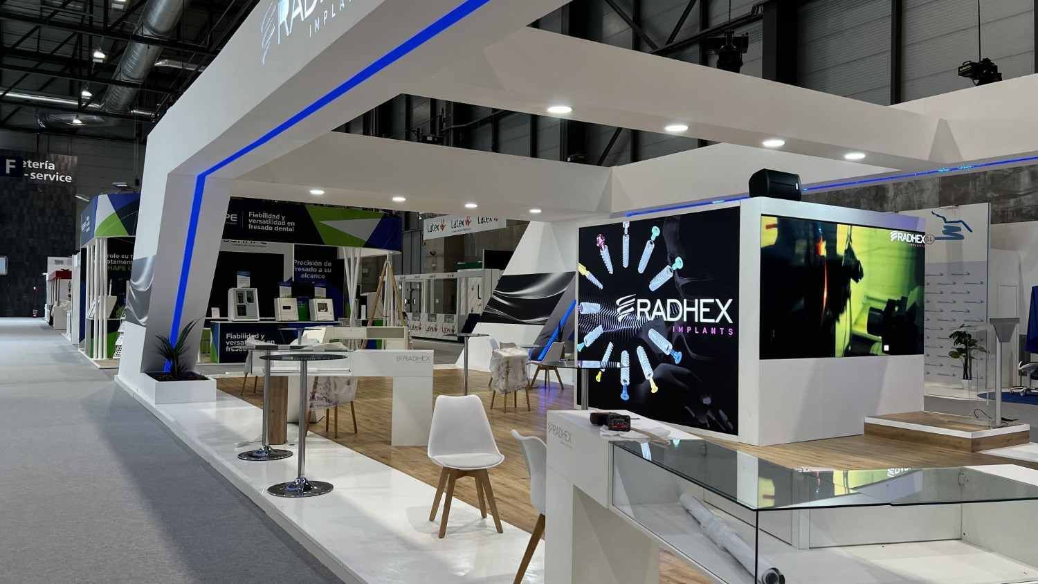 Moderno stand de feria con dosel blanco, mesas, sillas y la marca SpaceX en un centro de convenciones