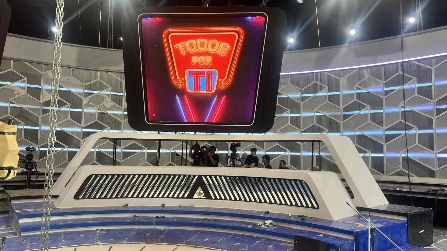 Platío de concurso de televisión con una gran pantalla central y un diseño futurista de escenario iluminado en azul