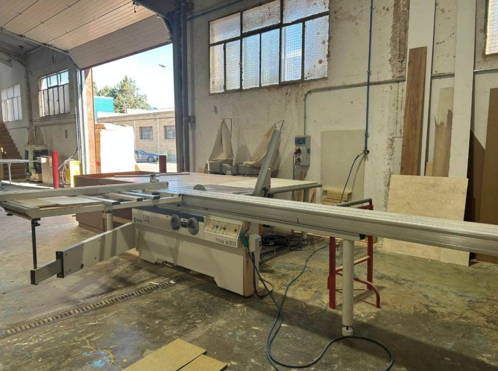 Taller industrial con una gran máquina de corte, una larga lámina de metal y ventanas a lo largo de la pared