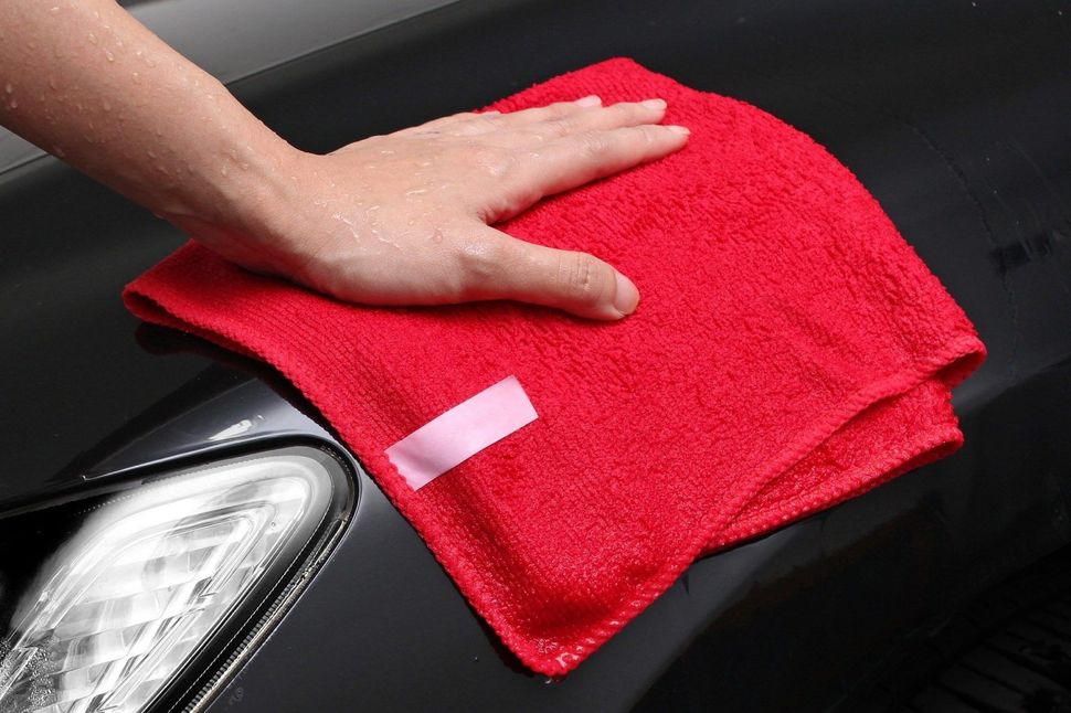 Eine Person putzt ein Auto mit einem roten Handtuch