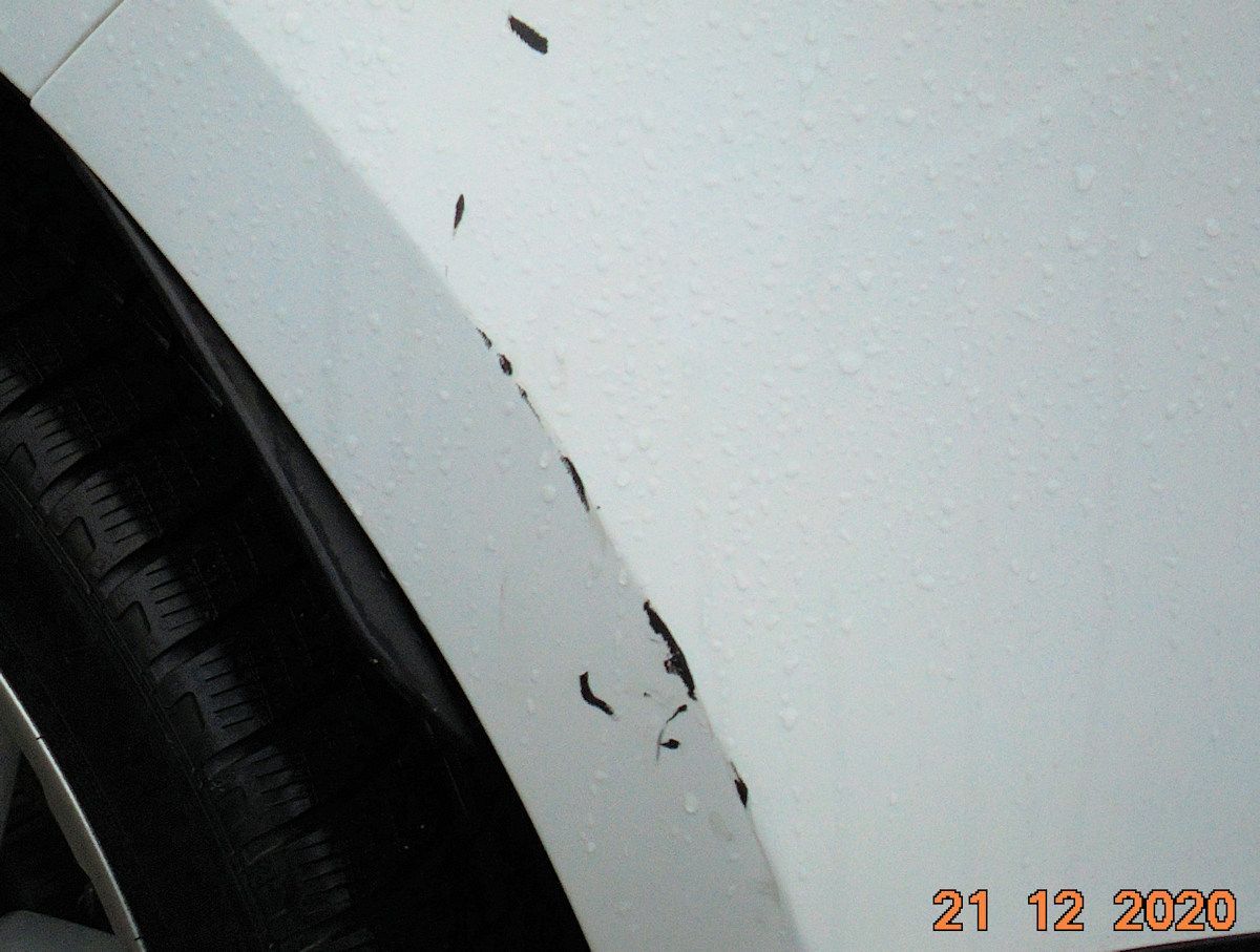 Ein Foto von einem weißen Auto mit Lackschäden am Kotflügel