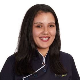 Mulher de cabelos longos e escuros, sorrindo, vestindo um uniforme azul-escuro com detalhes brancos.