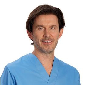 Homem de uniforme cirúrgico azul, cabelo castanho, sorrindo e olhando para a câmera.