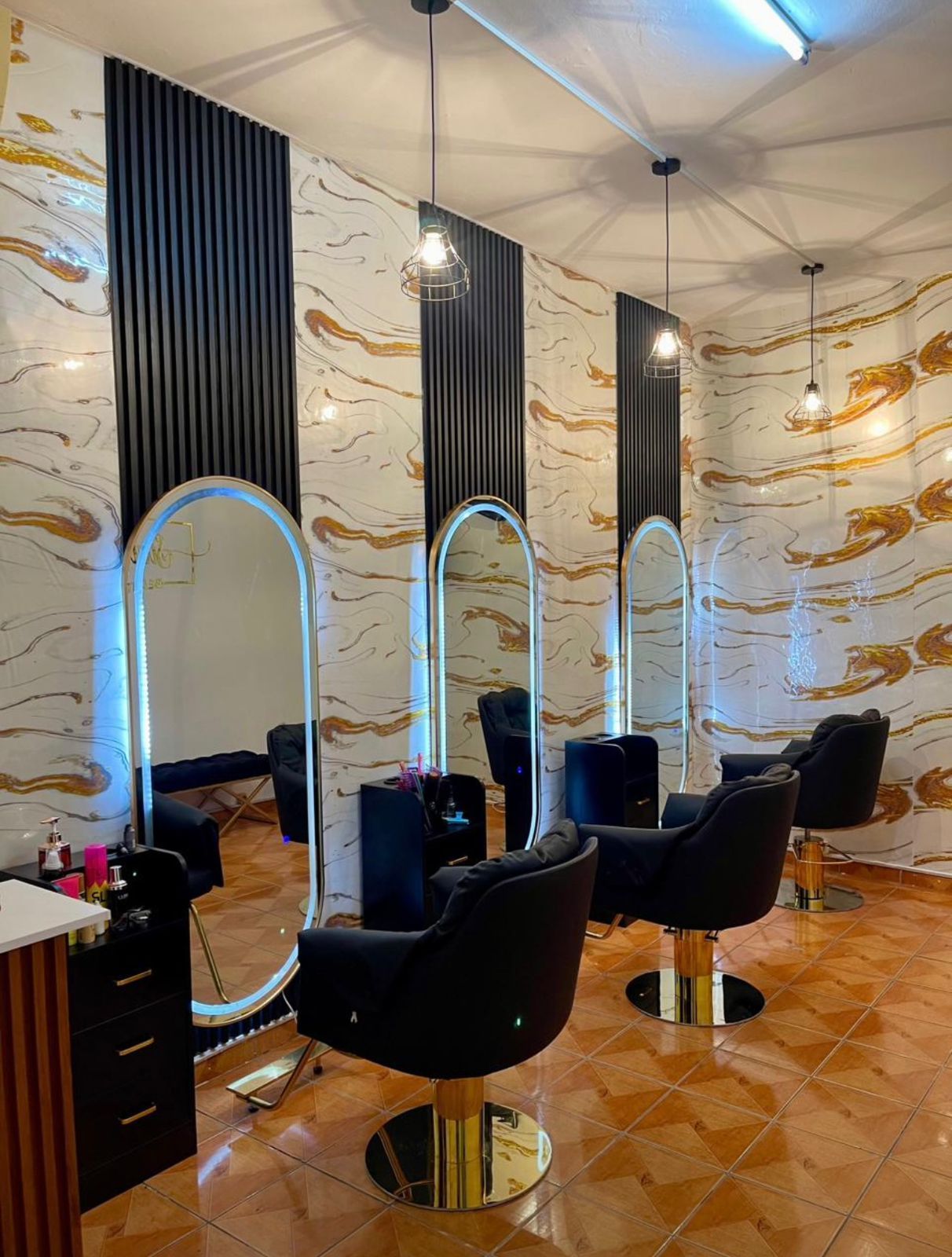Salão de beleza moderno com cadeiras de cabeleireiro pretas, espelhos e paredes com padrão de mármore.