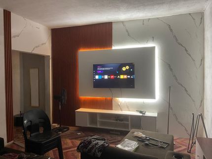 Sala de estar moderna com TV de parede, painel iluminado e poltrona preta.