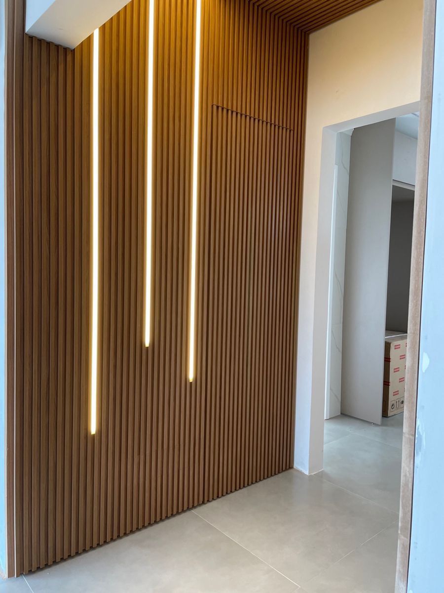 Hall de entrada moderno com ripas de madeira verticais e estreitas faixas de luz embutidas ao lado da porta.