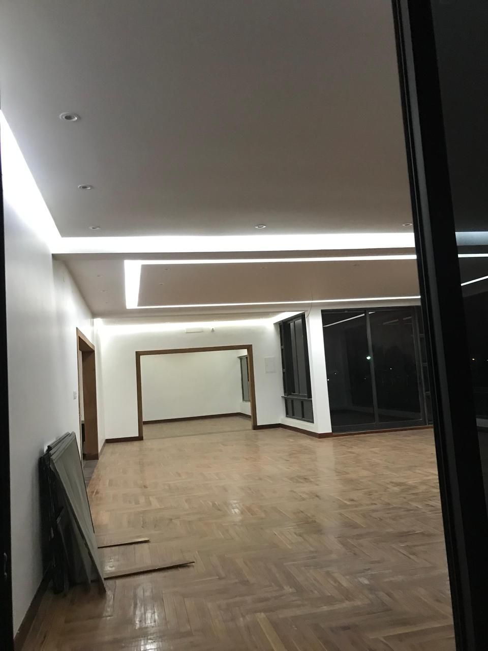Quarto moderno e vazio com piso de madeira, iluminação embutida no teto e grandes portas de vidro escuro.