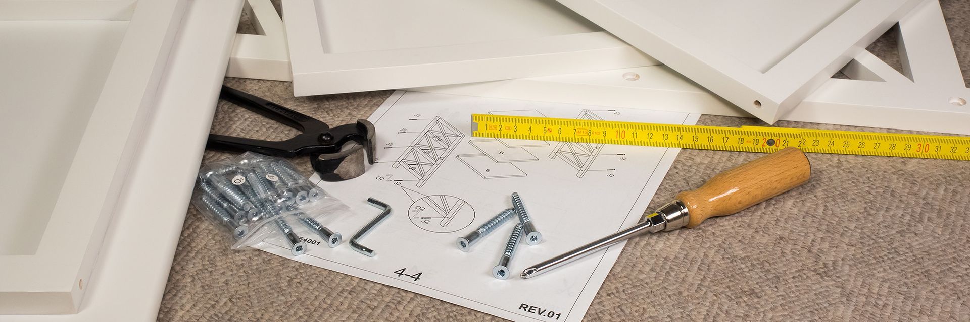 Auf dem Boden liegen ein Haufen Schrauben, Nägel und ein Maßband.