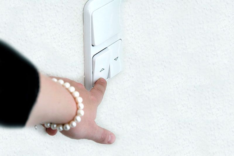 Eine Person, die ein Perlenarmband trägt, drückt einen Knopf an einem Lichtschalter.