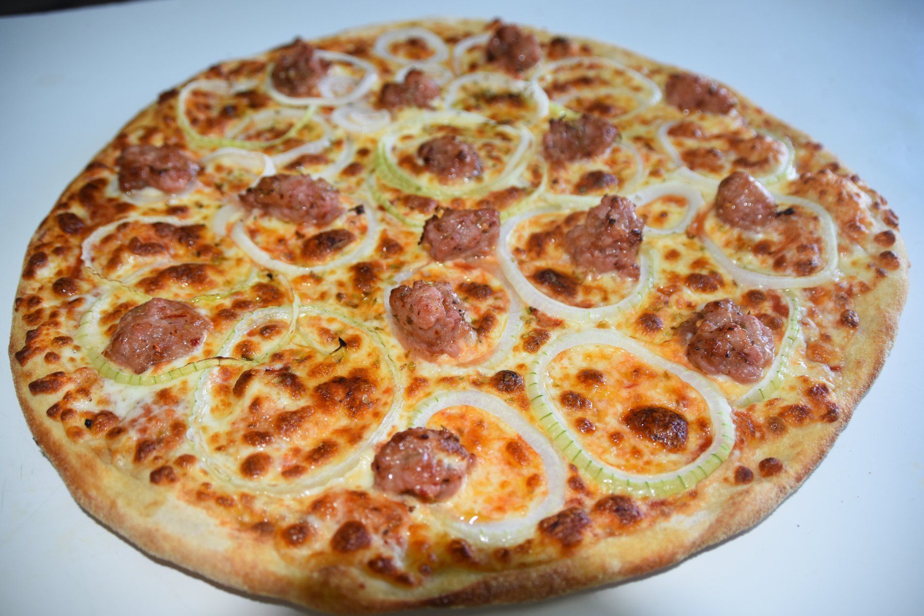 Pizza cubierta con cebolla y salchicha, sobre una superficie blanca.