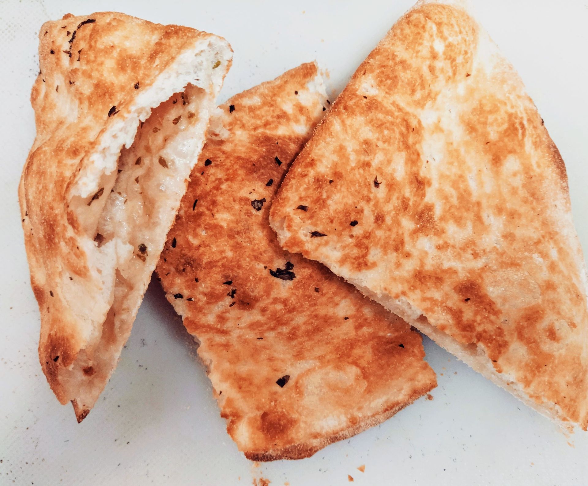 Tres rebanadas de pan plano tostado con hierbas. El pan está dorado y ligeramente quemado.