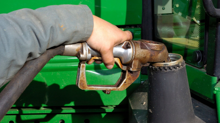 Pompage manuel du carburant dans un tracteur vert ; buse rouillée tenue près du réservoir de carburant.